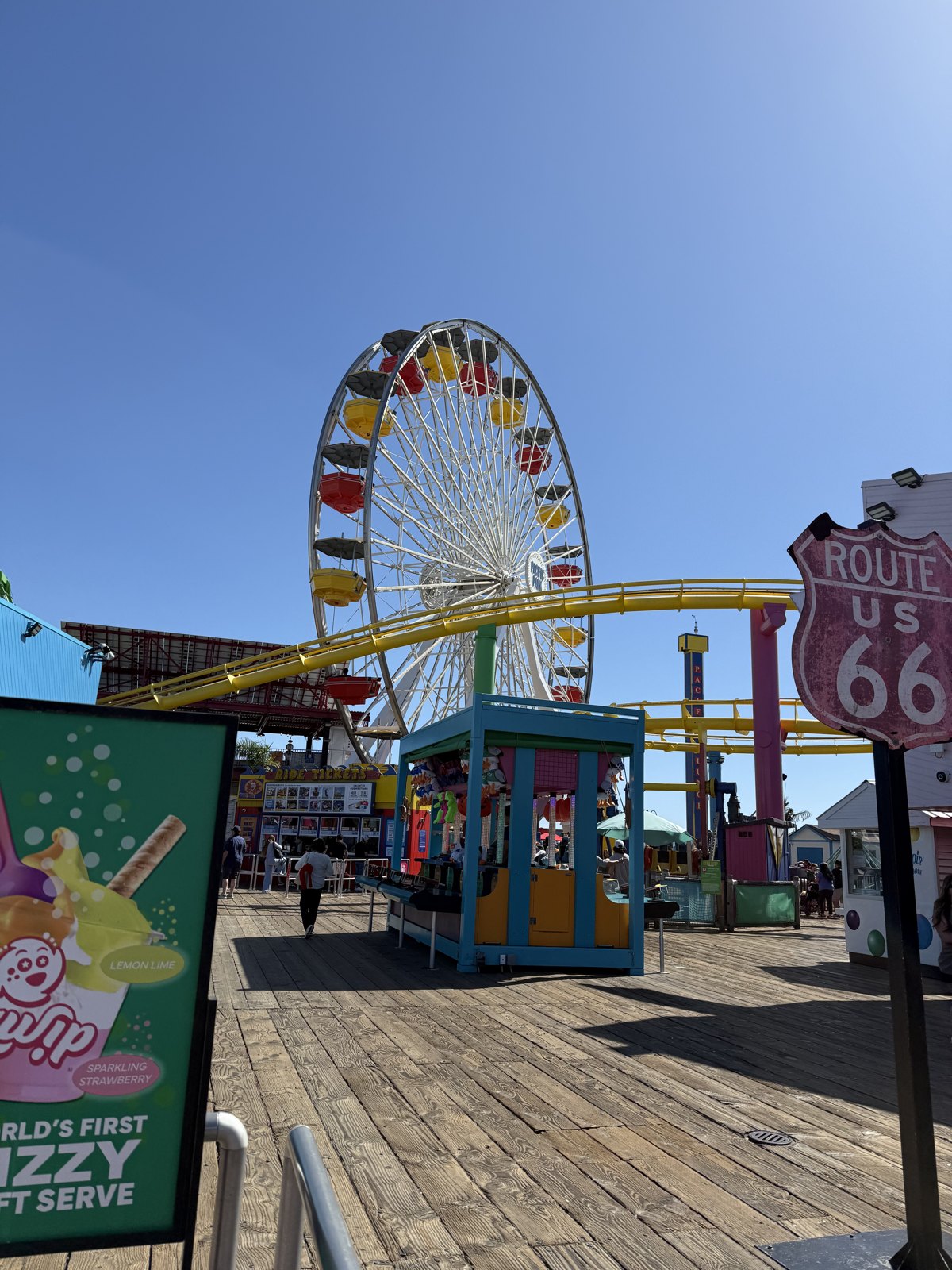 Santa Monica Pier at dusk — the Pacific Park ferris wheel lit up beside the Route 66 end-of-the-trail sign