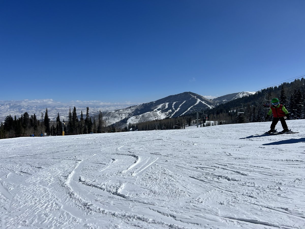A wide groomed ski slope in Park City under a clear blue sky, mountains in the distance